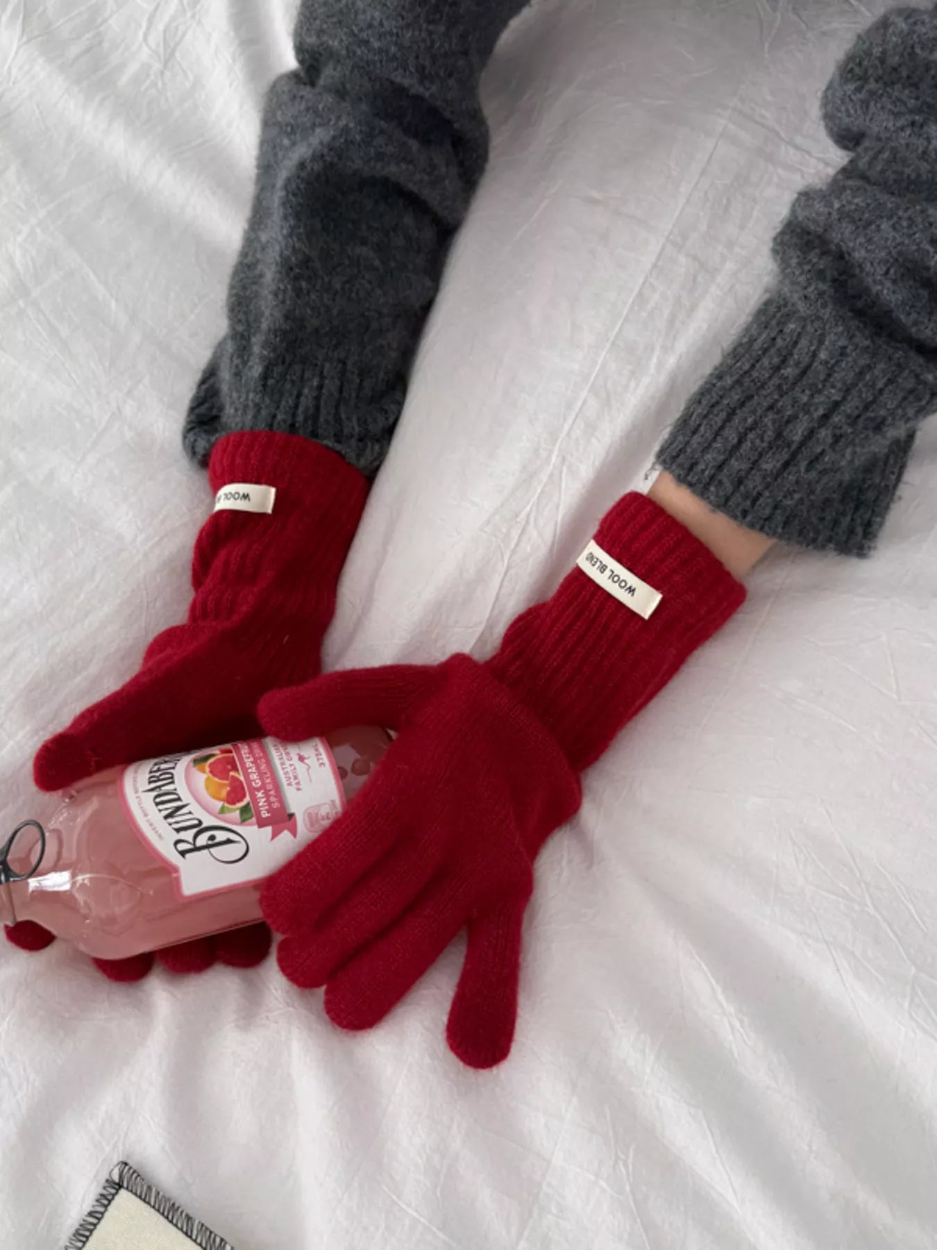 Red gloves holding a bottle of pink lemonade on a white surface