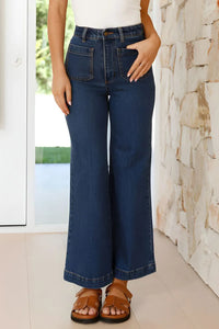 Person wearing blue wide-leg jeans standing indoors against a stone wall.