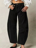 Person wearing black wide-leg jeans with a white blouse against a neutral background