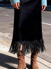 Person wearing a black fringe skirt with brown boots on a street.