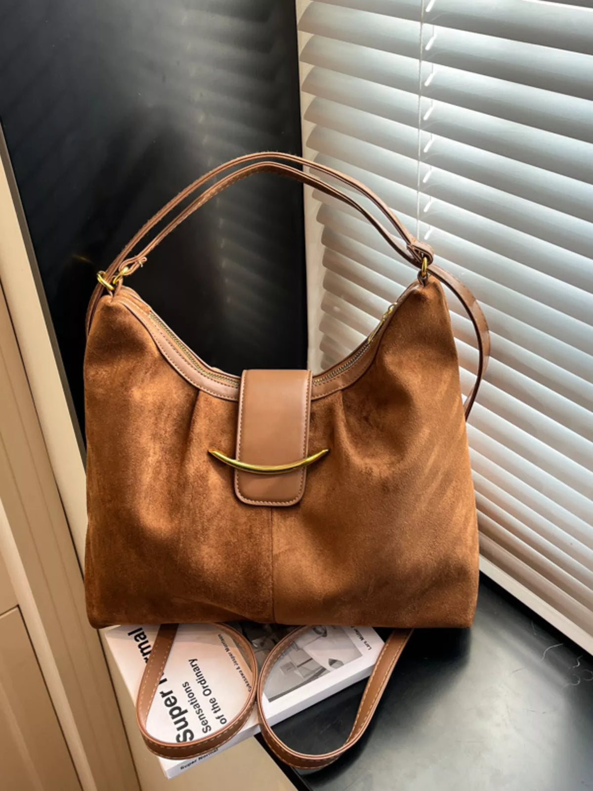 Brown leather handbag on a surface with blinds in the background