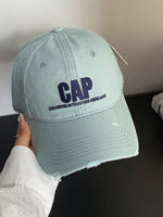 Light blue cap with 'CAP' and text held by a person against a neutral background