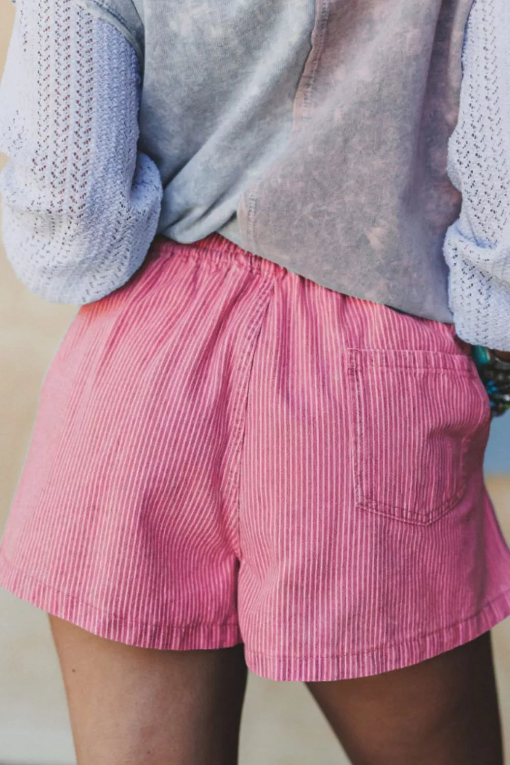 Person wearing pink shorts and a light blue sweater with a textured pattern.