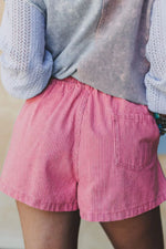 Person wearing pink shorts and a light blue sweater with a textured pattern.