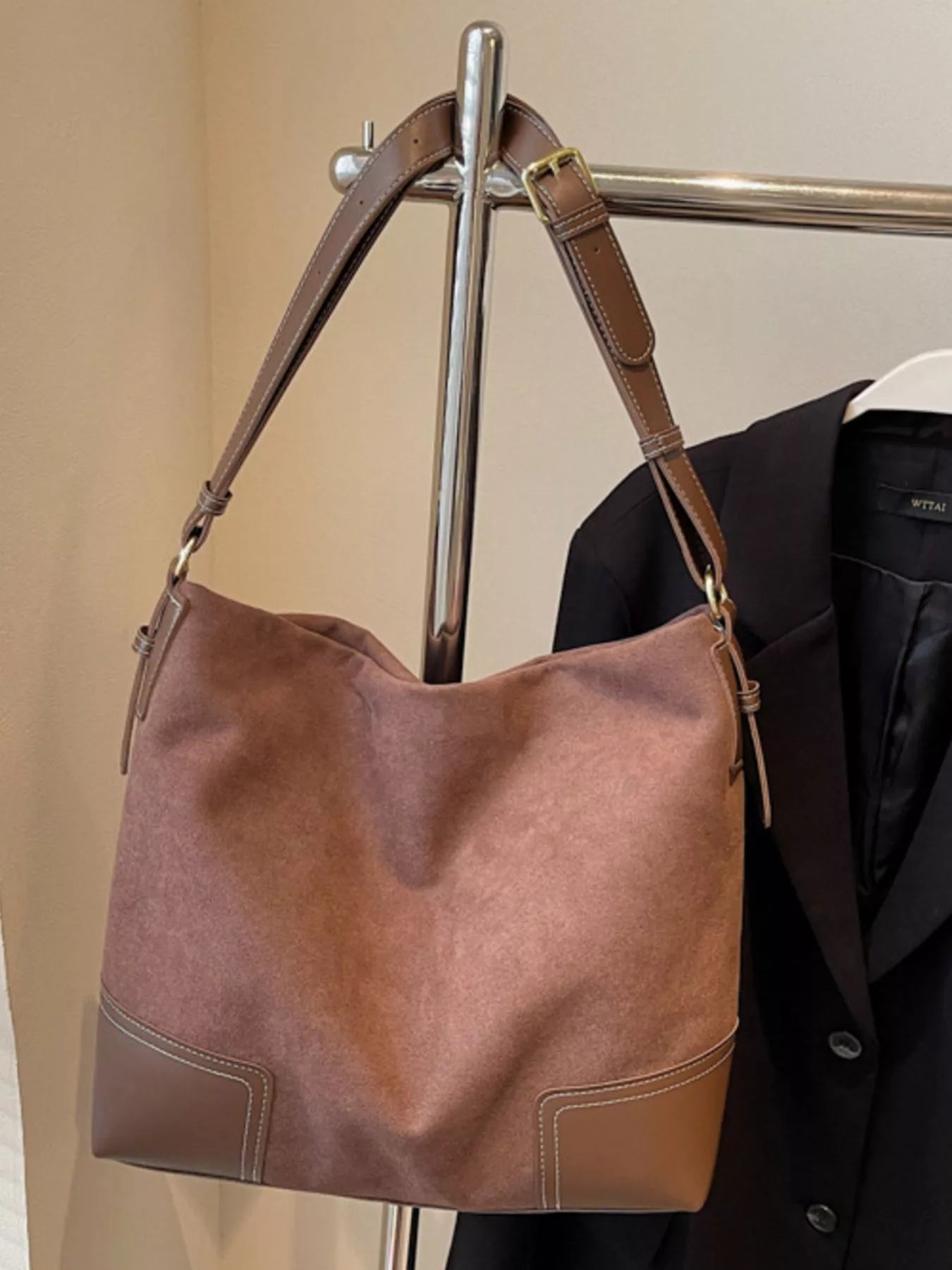 Brown leather handbag hanging on a rack with a beige wall background