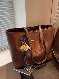 Brown leather tote bag with a keychain on a surface