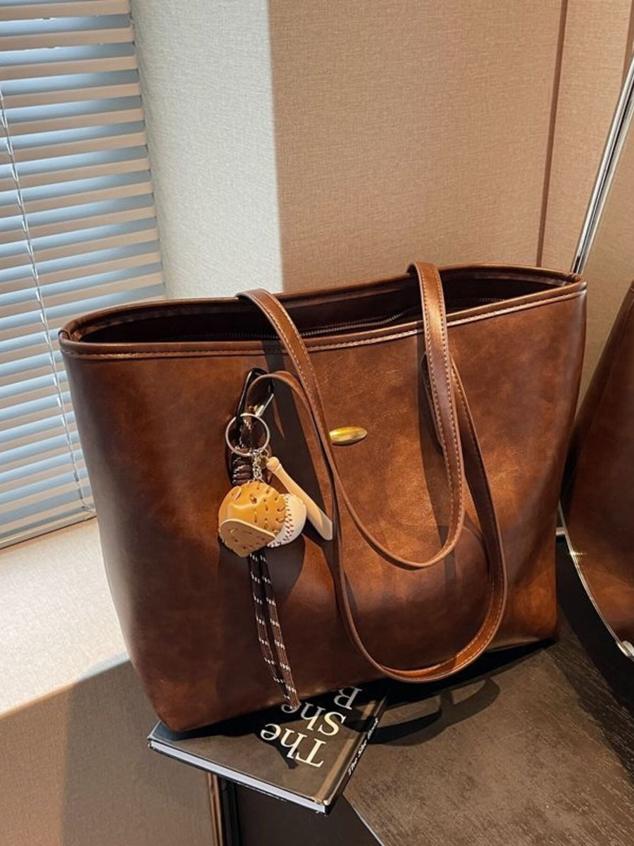 Brown leather tote bag with a keychain on a surface