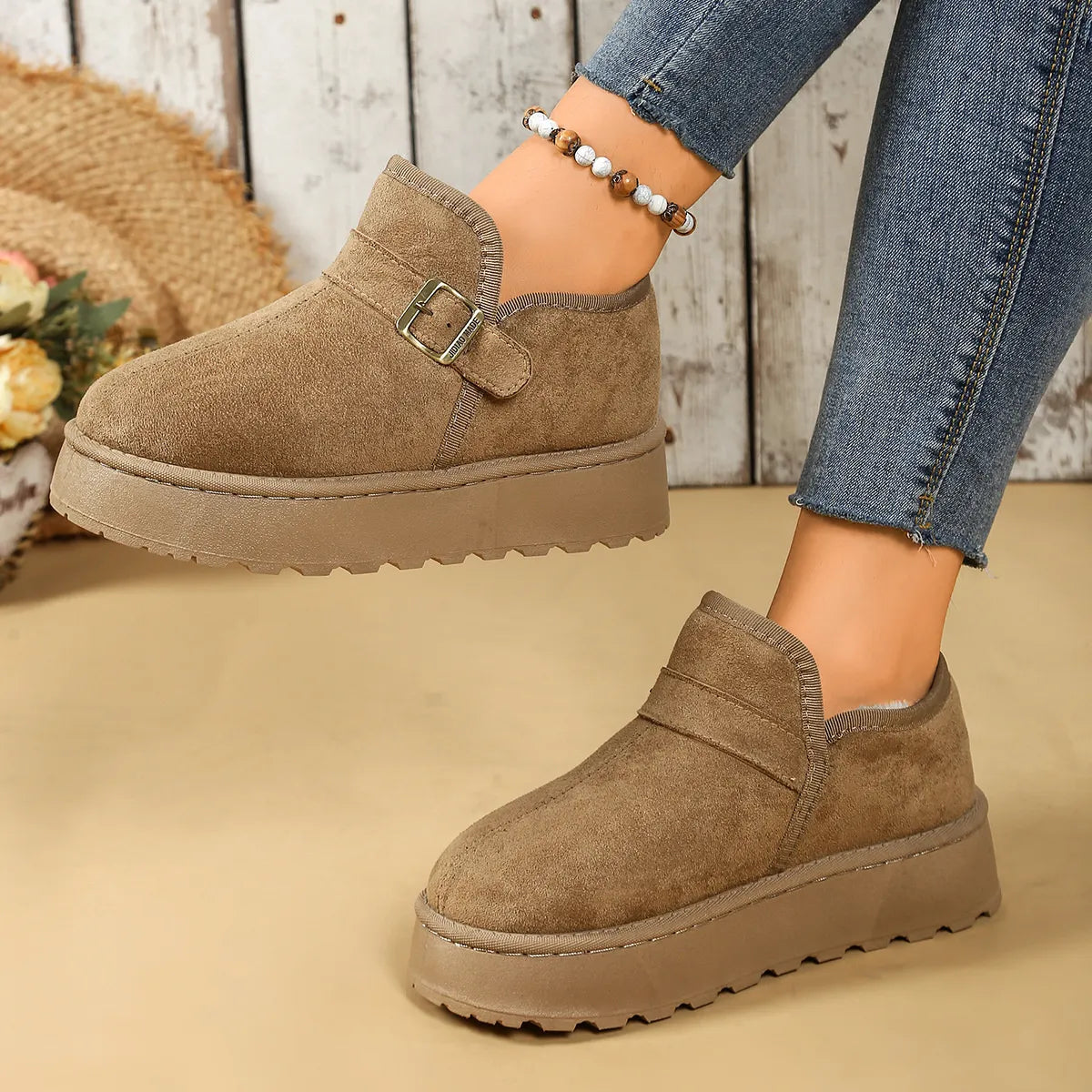 Brown suede shoes with buckles worn by a person, on a beige background