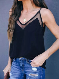 Person wearing a black tank top with sheer mesh panels and ripped blue jeans against a gray background