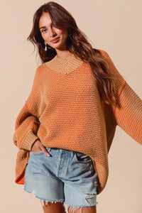 Woman wearing an orange sweater and denim shorts against a beige background