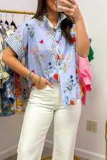 Person wearing a colorful floral shirt and white pants in a clothing store.
