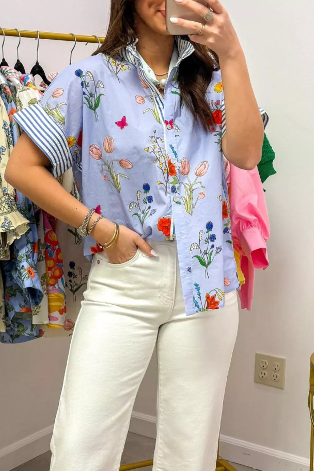 Person wearing a colorful floral shirt and white pants in a clothing store.