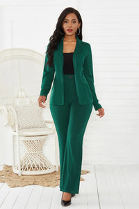 Woman wearing a green suit standing in a minimalistic room with a white chair and light-colored floor.