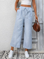 Person wearing blue and white striped wide-leg pants with a white top and white sneakers, standing against a light gray wall.
