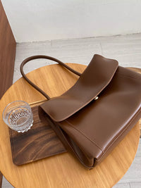 Brown leather handbag on a wooden table with a glass of water