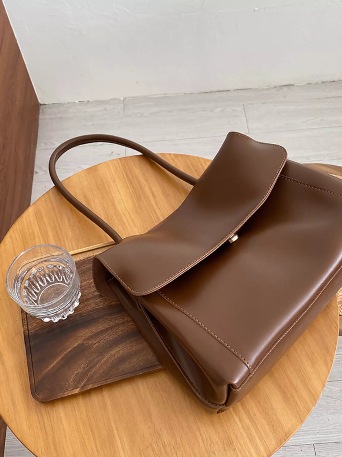 Brown leather handbag on a wooden table with a glass of water