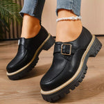 Black leather shoes with a buckle on a wooden floor