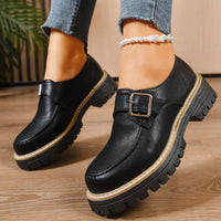 Black leather shoes with a buckle on a wooden floor