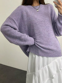 Person wearing a light purple sweater and white pants against a plain background