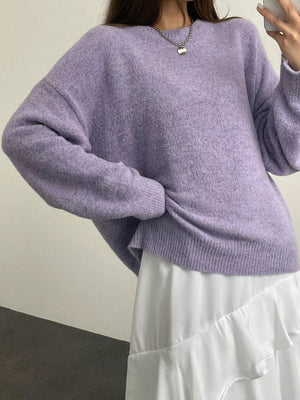 Person wearing a light purple sweater and white pants against a plain background
