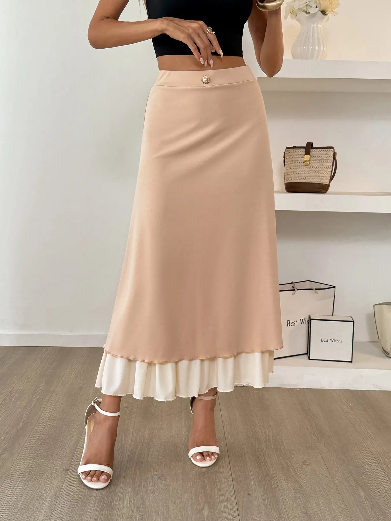 Person wearing a beige skirt with a white hem in a minimalistic setting.