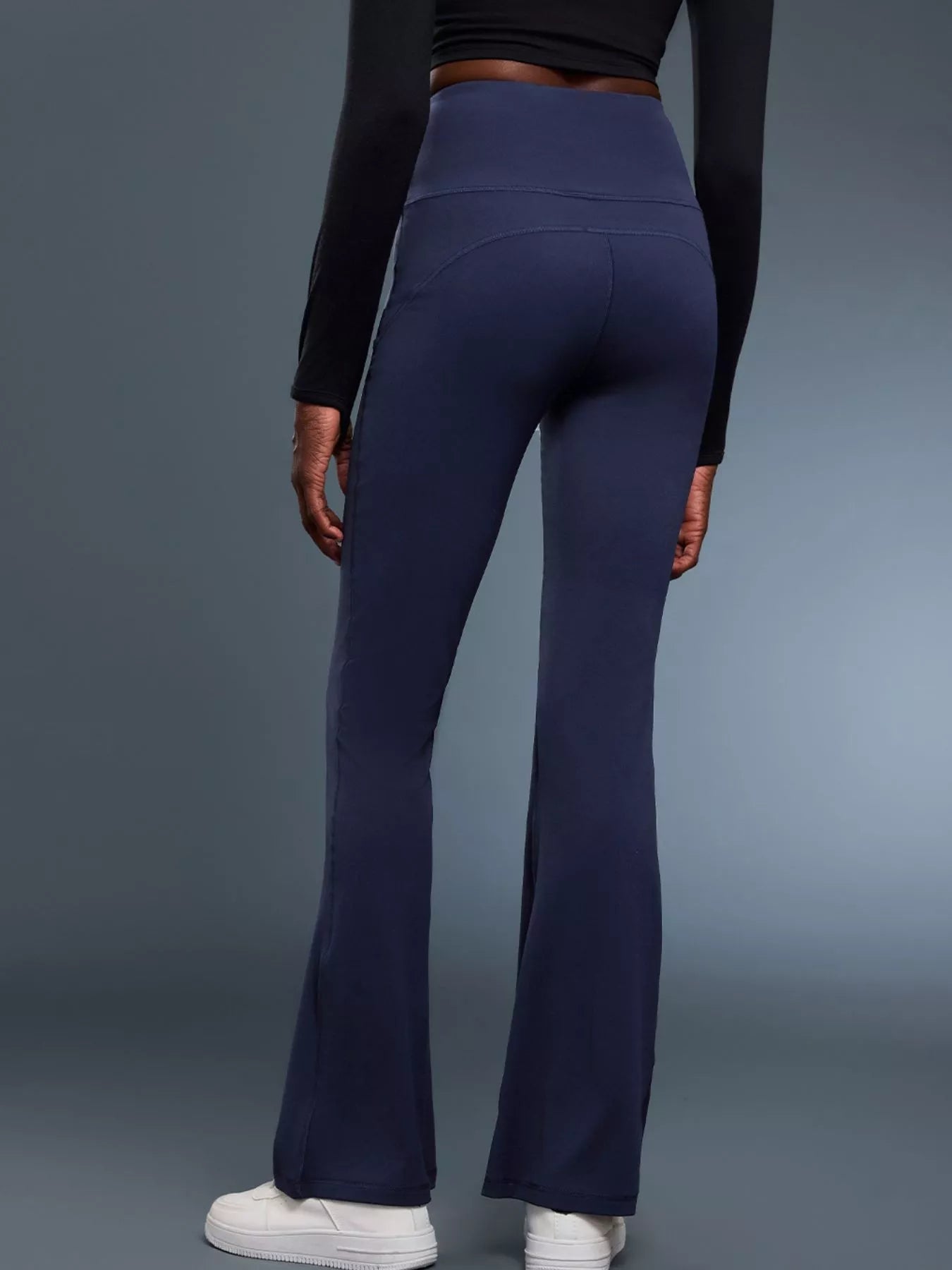 Person wearing navy flared pants and a black long-sleeve top on a gray background