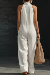 Person wearing a white jumpsuit holding a woven bag against a dark background