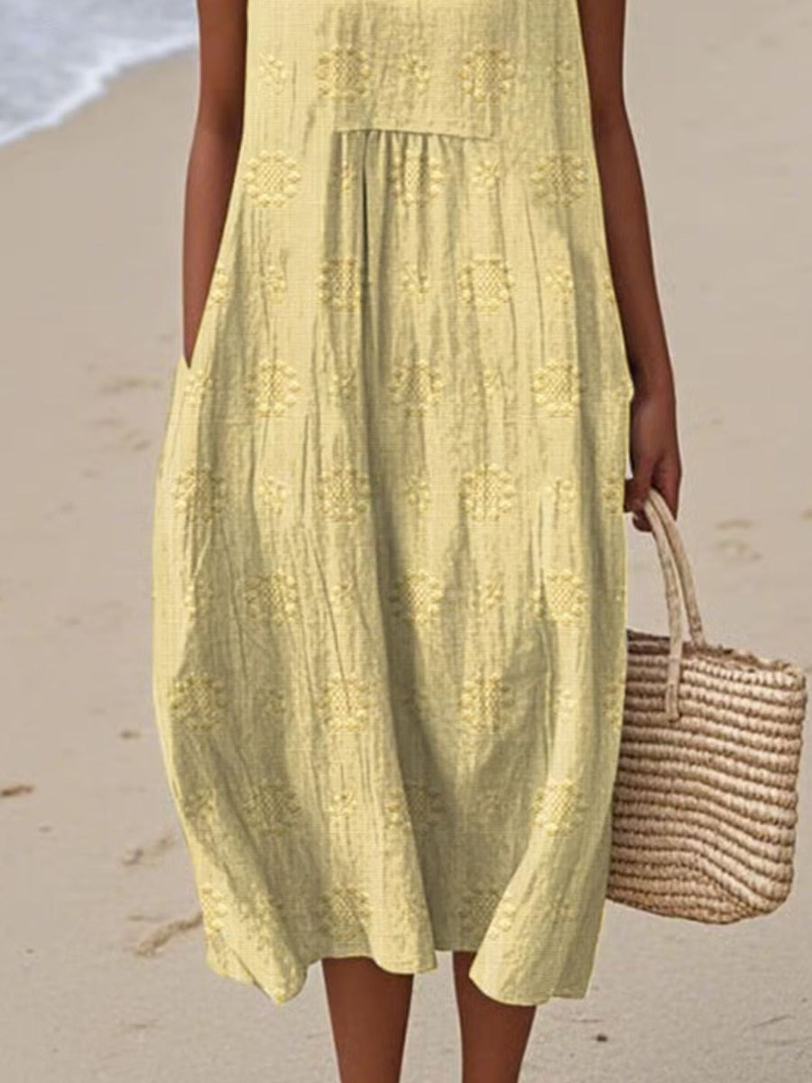 Person wearing a yellow dress on a beach holding a straw bag.