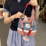 Person holding a small checkered bag with a phone case attached, in an indoor setting.