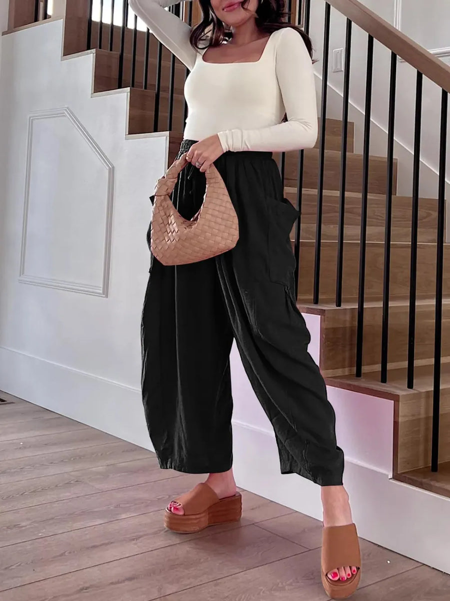 Woman holding a woven handbag in a home setting with stairs in the background