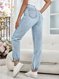 Person wearing light blue jeans and white sneakers in a bright room with flowers and a couch.