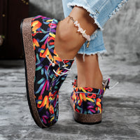 Colorful floral-patterned shoes worn with denim shorts on a gray surface.
