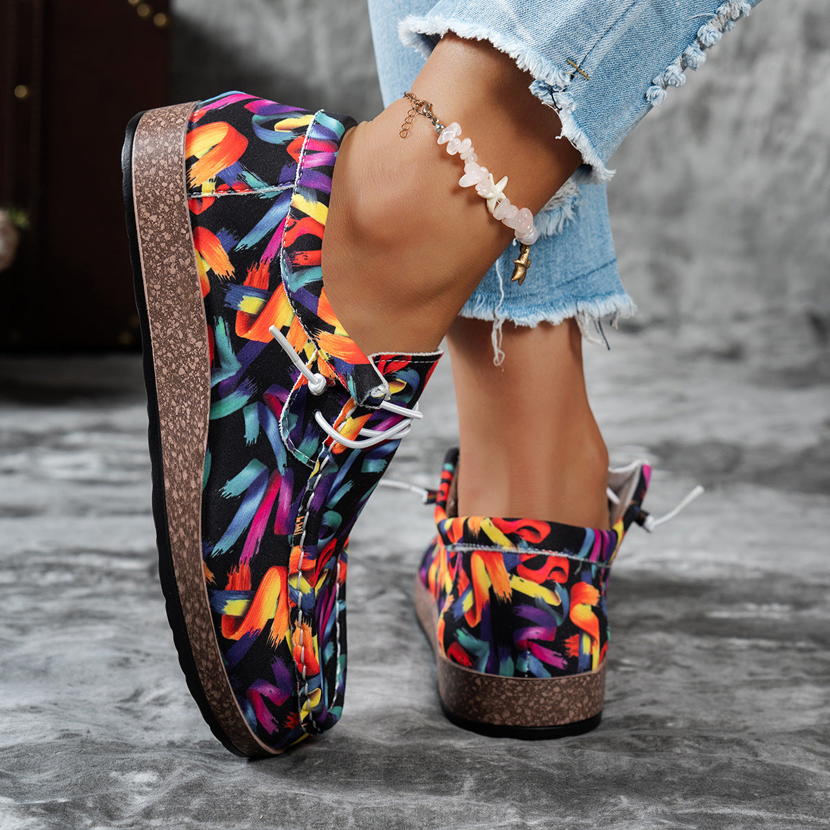 Colorful floral-patterned shoes worn with denim shorts on a gray surface.