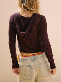 Person wearing a dark purple hoodie with lace details on a plain background