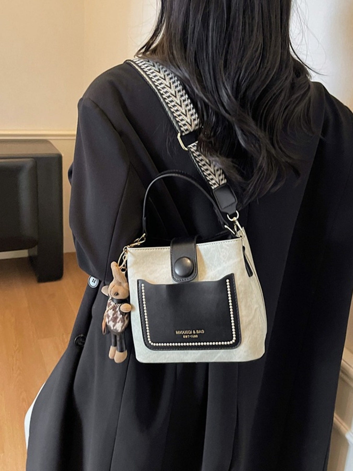 Person wearing a black coat with a beige and black handbag on a neutral background