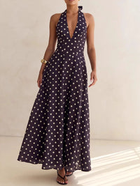 Woman wearing a long navy dress with white polka dots on a neutral background