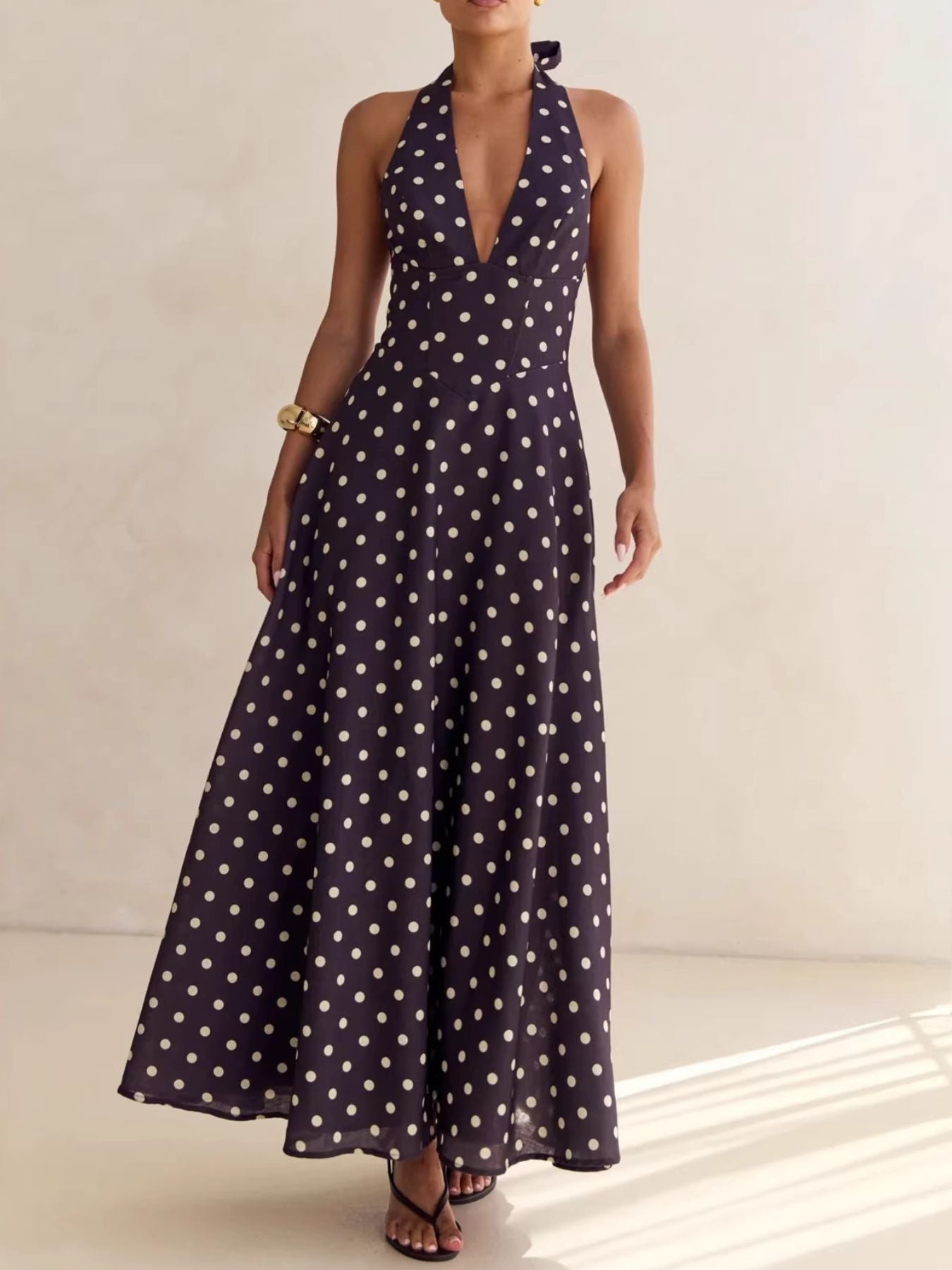 Woman wearing a long navy dress with white polka dots on a neutral background