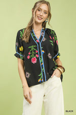 Woman wearing a black blouse with colorful floral embroidery on a light green background