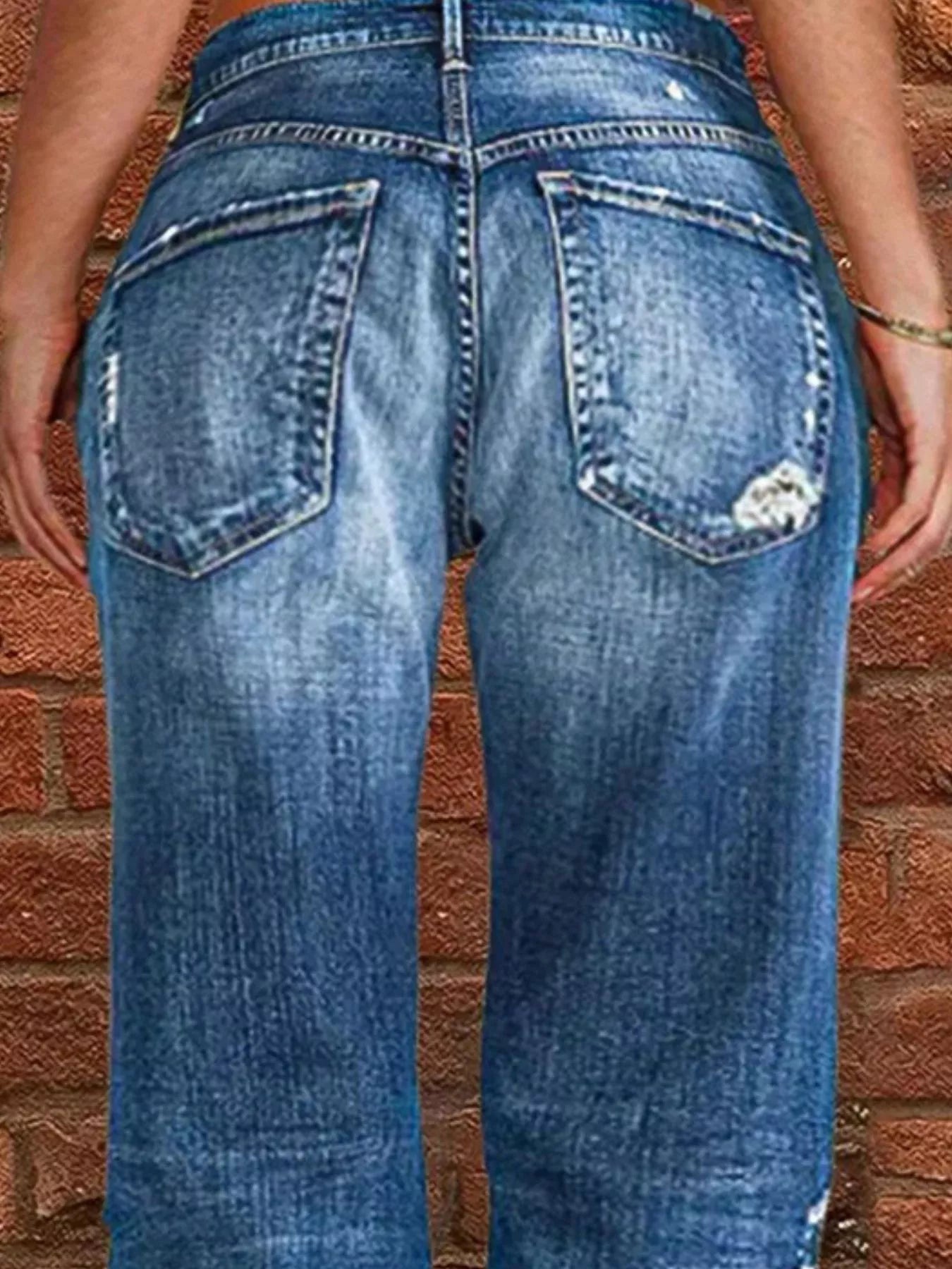 Blue jeans with a distressed look worn by a person against a brick wall.
