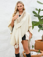 Woman wearing a cream-colored poncho with fur trim in front of a white wall and potted plant.
