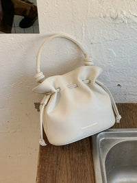 White drawstring bag on a wooden surface with a white wall background