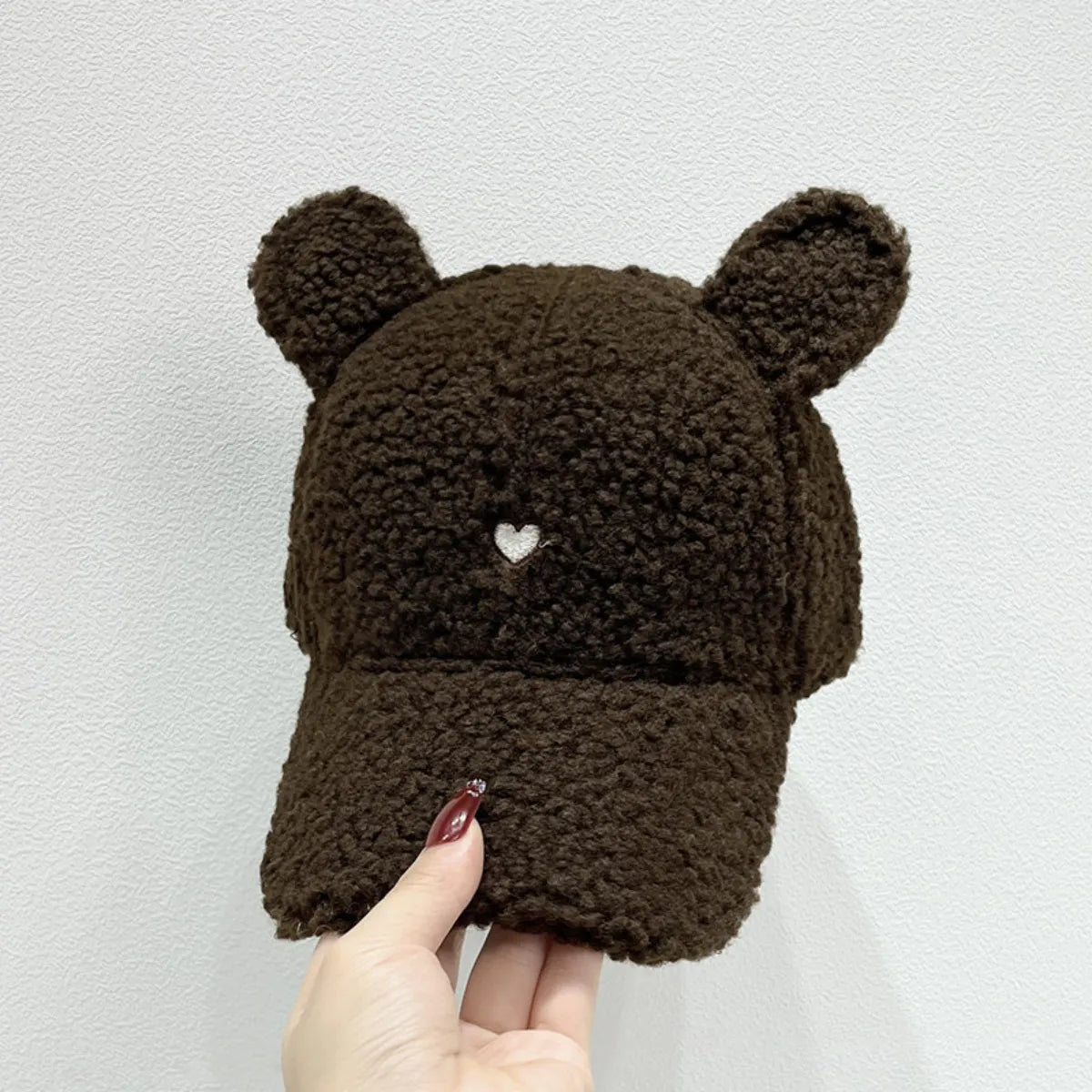Brown teddy bear-shaped hat held by a hand against a light gray background