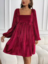 Woman wearing a burgundy pleated dress with long sleeves in an indoor setting.
