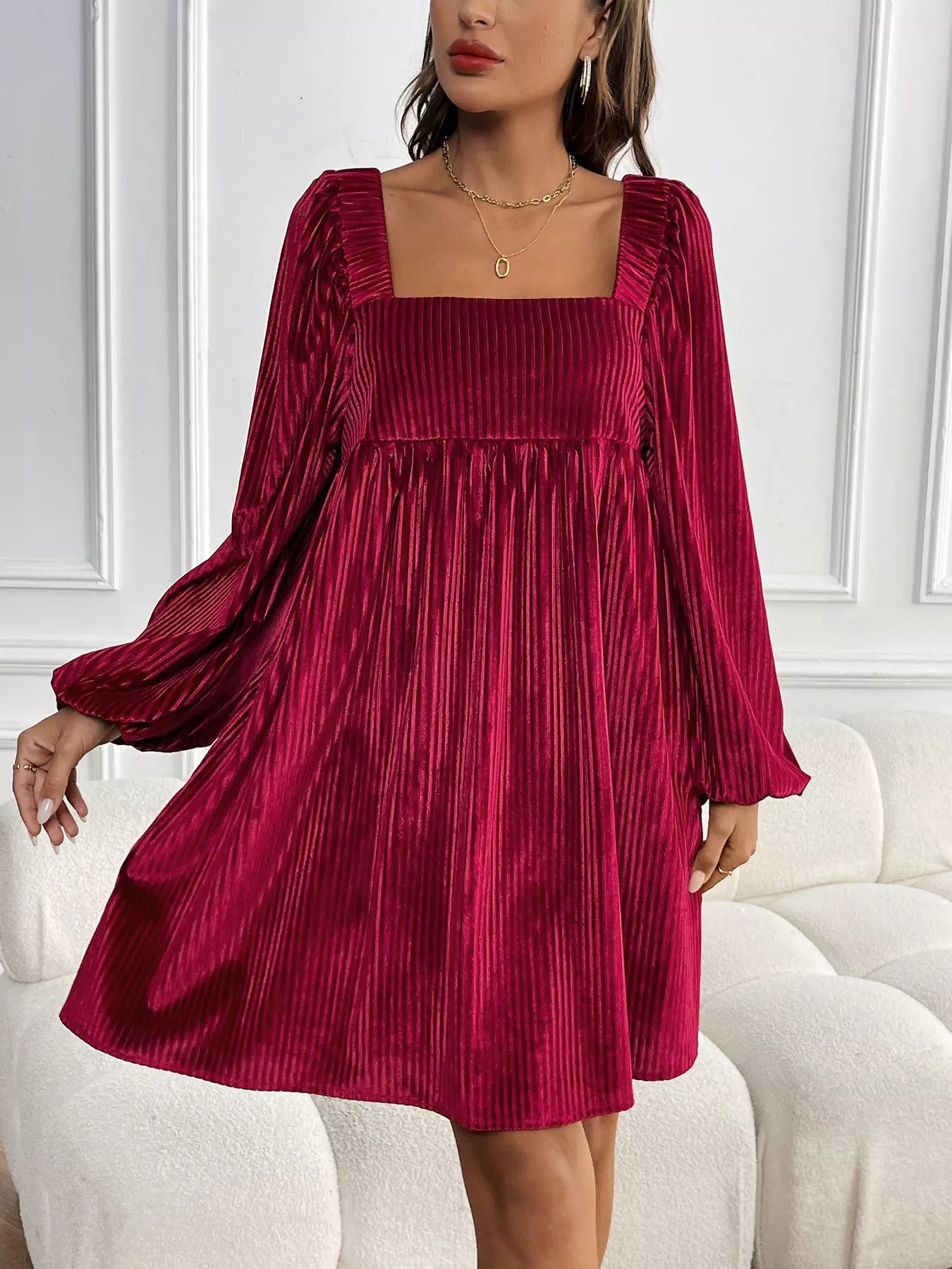 Woman wearing a burgundy pleated dress with long sleeves in an indoor setting.