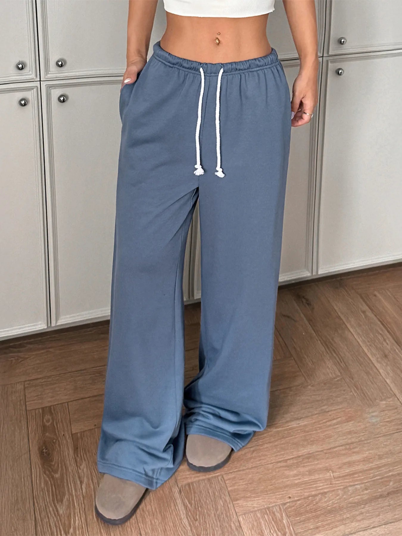 Person wearing blue sweatpants with a white top in a room with wooden flooring and gray cabinets.