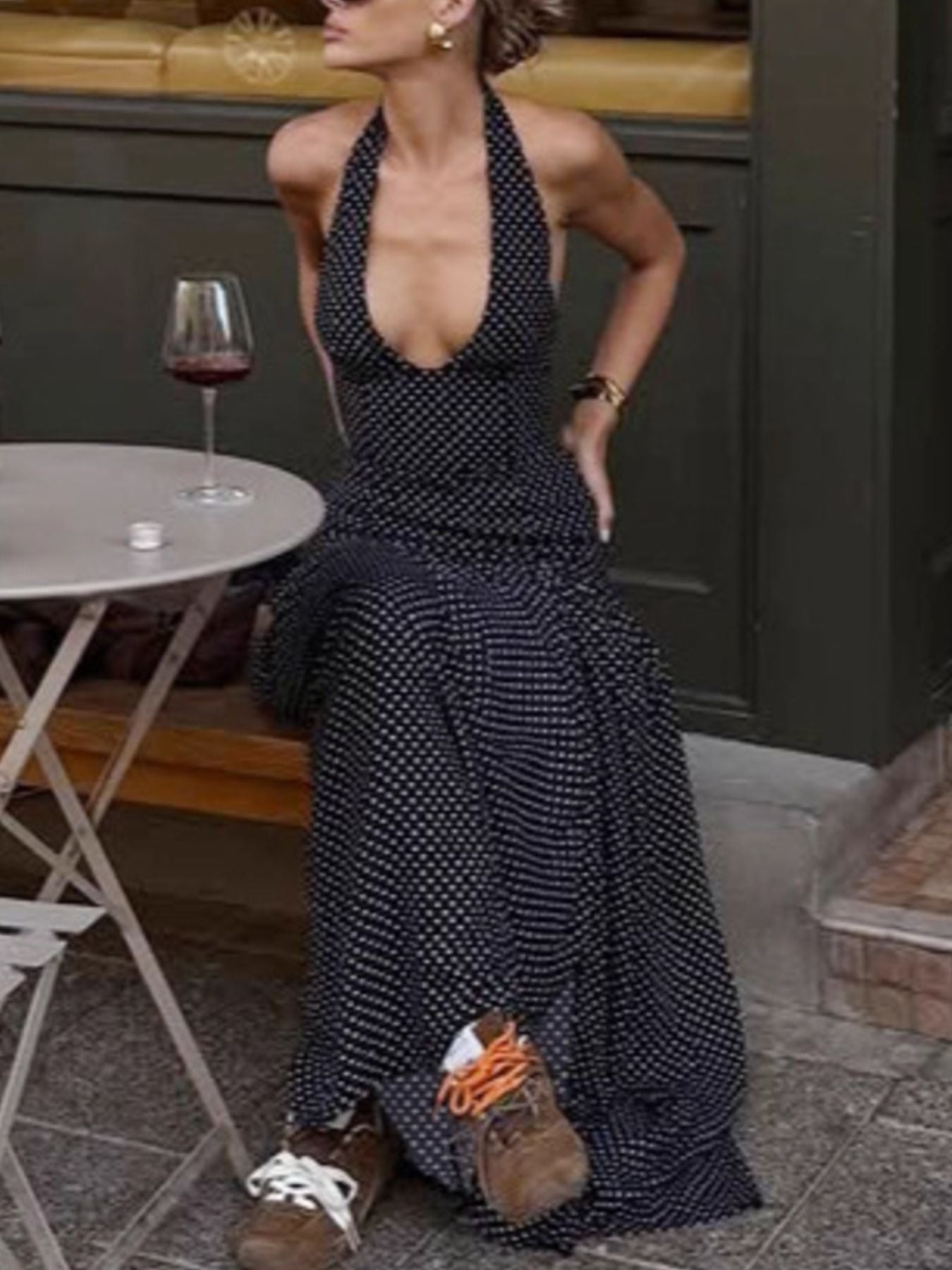 Woman in a black patterned dress sitting outdoors with a glass of wine.