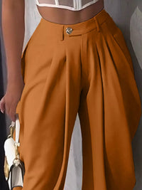 Brown pleated pants worn by a person against a neutral background
