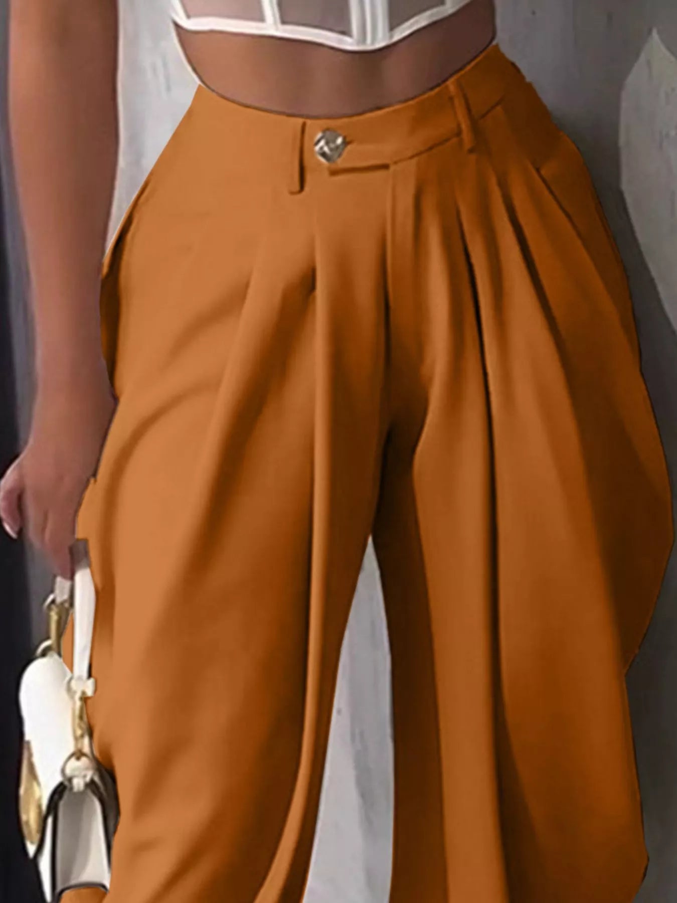 Brown pleated pants worn by a person against a neutral background