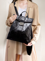Person holding a black leather backpack against a neutral background