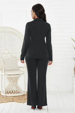 Woman wearing a black suit standing in a minimalistic room with a white chair and light-colored floor.